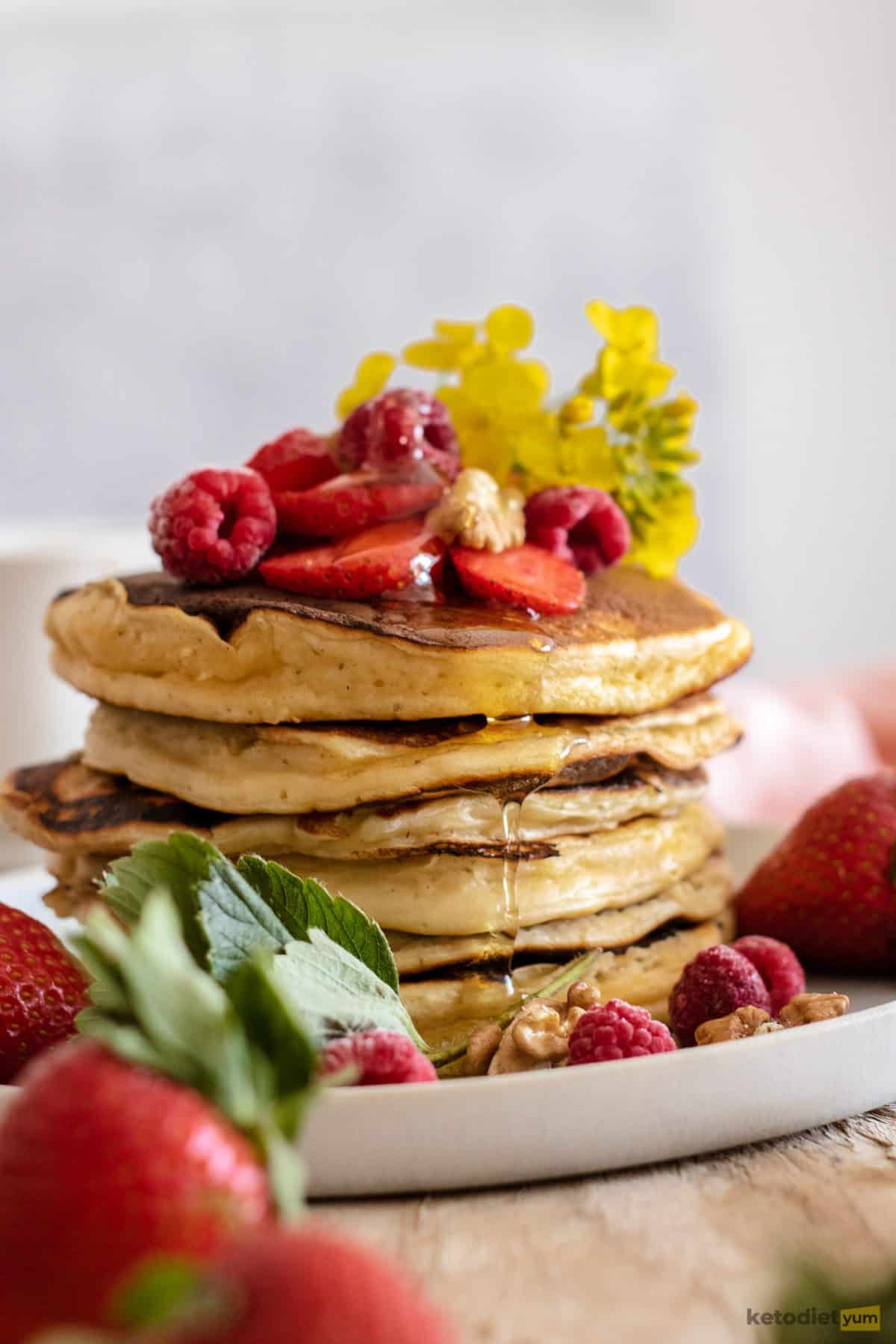 A fresh stack of low carb pancakes topped with raspberries and sugar-free maple syrup