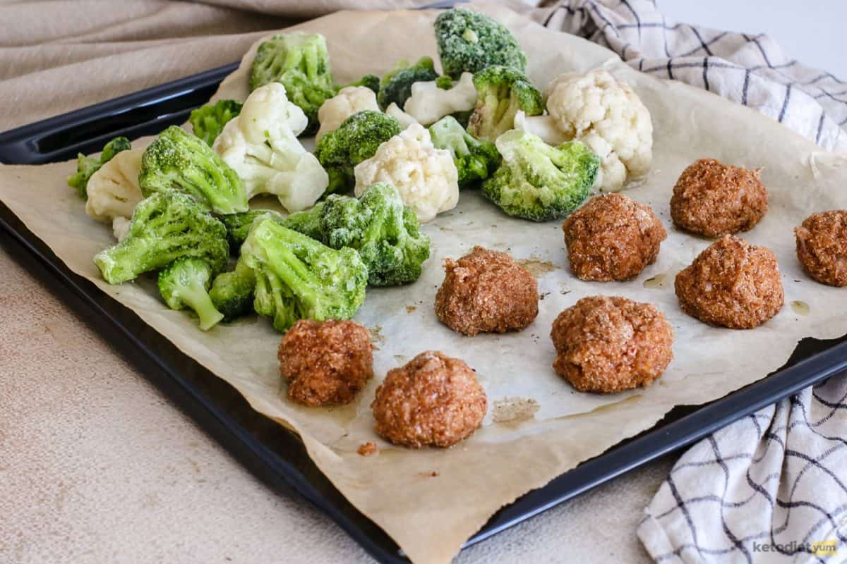 Low carb chicken meatballs with broccoli and cauliflower florets on a baking tray ready to bake