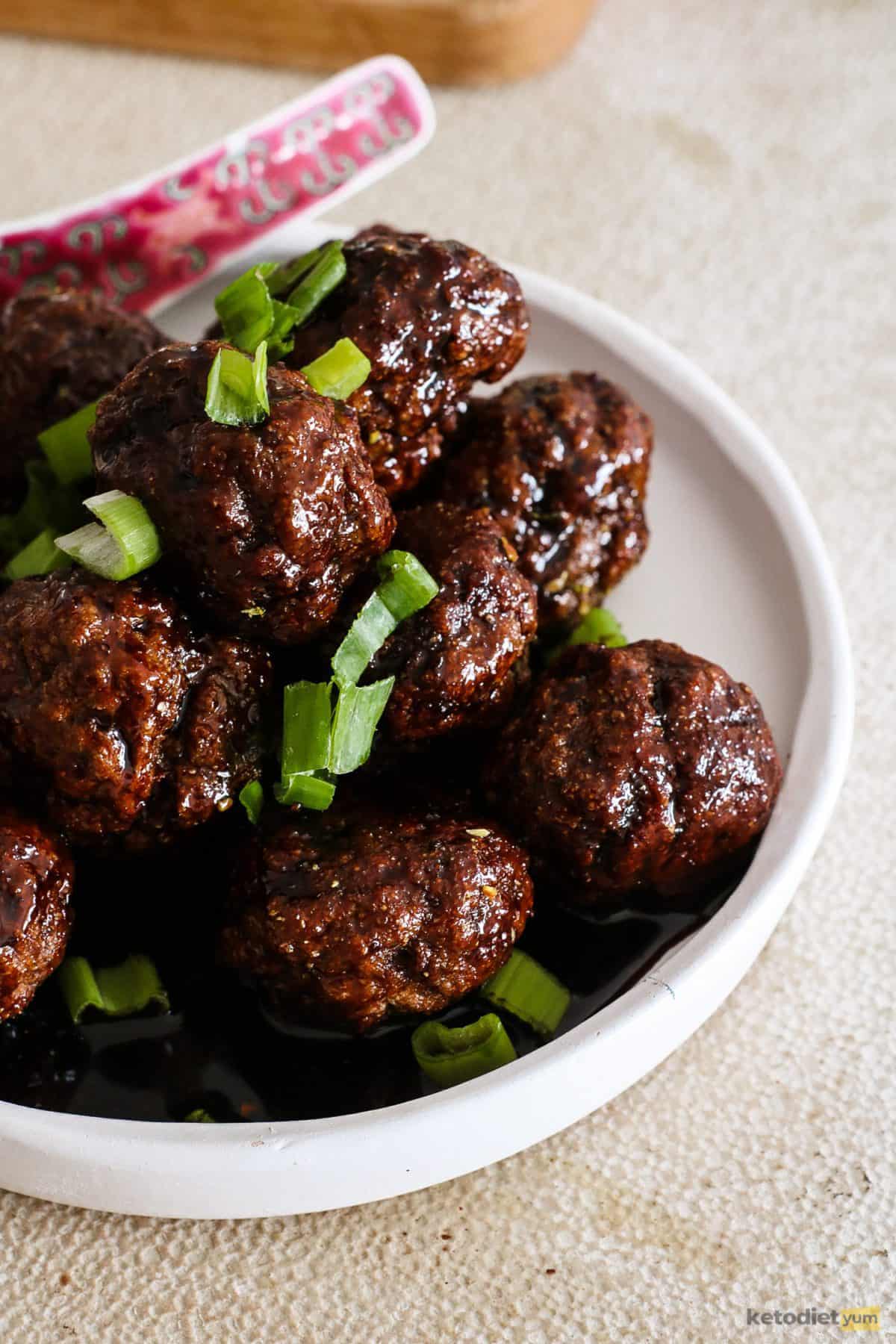 A bowl of savory and sticky keto Kung Pao meatballs garnished with diced green onion and ready to eat