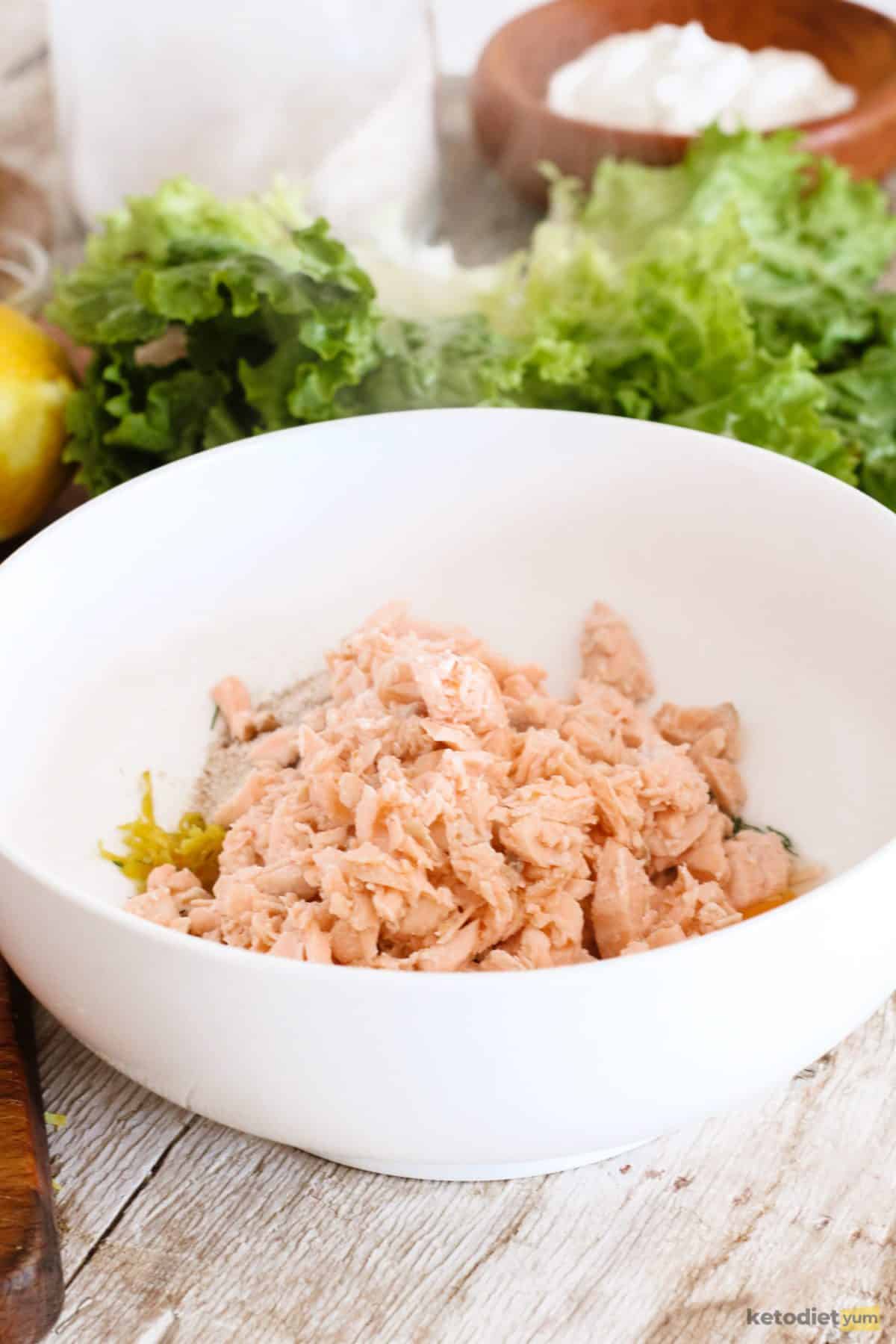 Flaked salmon in a white bowl ready to combine with other ingredients into burgers