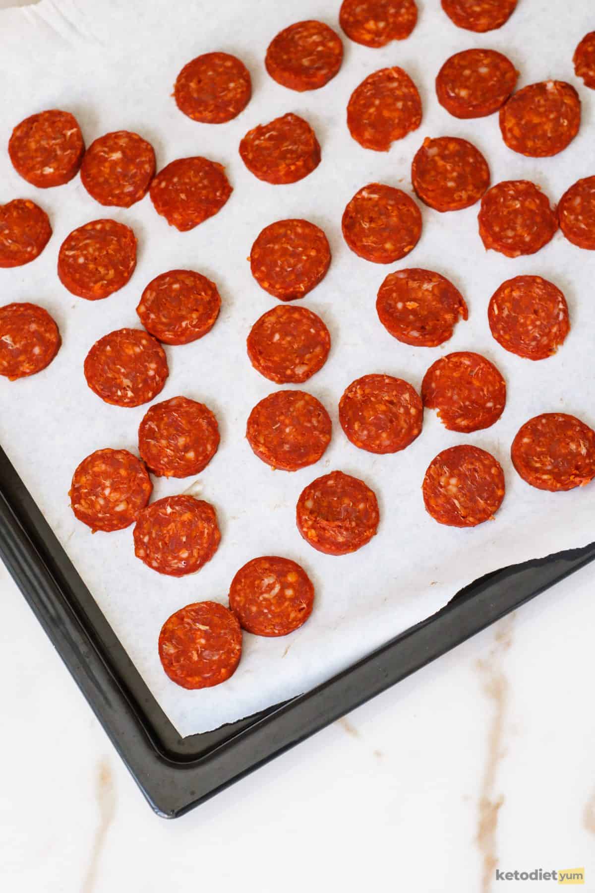 Sliced chorizo chips on a baking pan lined with baking paper ready to bake in the oven