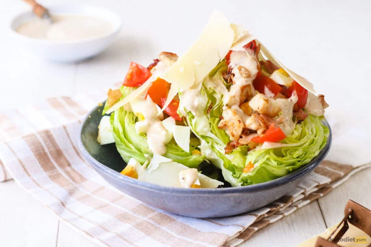 Loaded Caesar Wedge Salad in a blue bowl made with iceberg lettuce wedges topped with chicken, bacon, cherry tomatoes, a homemade dressing and fresh parmesan