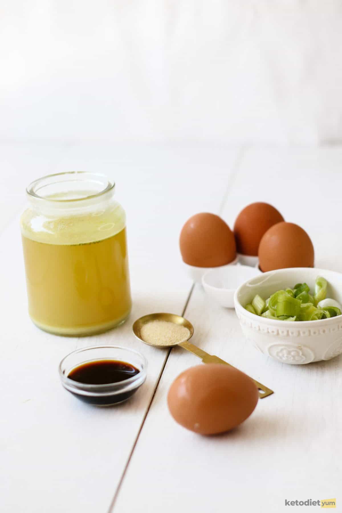 Ingredients on a table for this egg drop soup recipe including eggs, green onion, broth, coconut aminos and ginger
