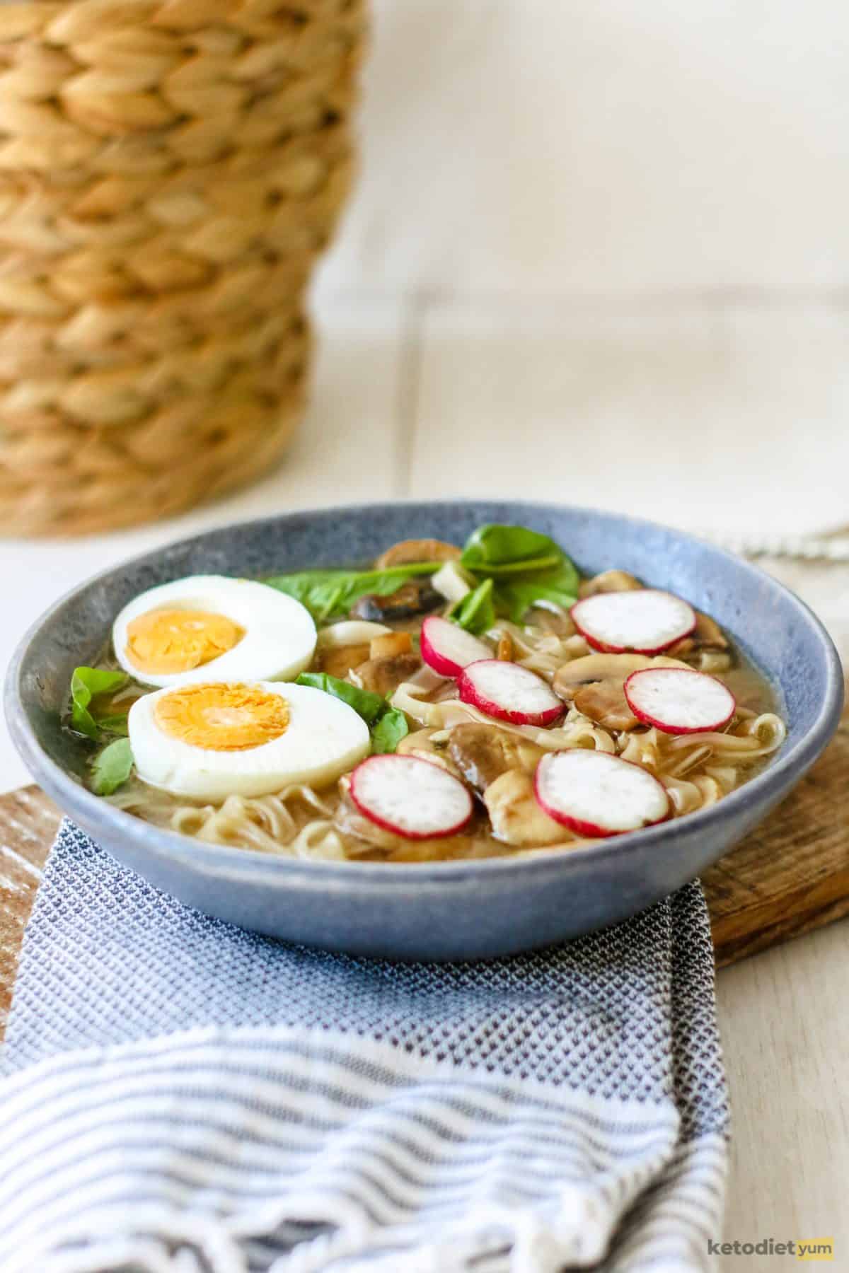 A delicious bowl of keto ramen noodle soup made with shirataki noodles, spinach and mushrooms and topped with sliced egg and radish