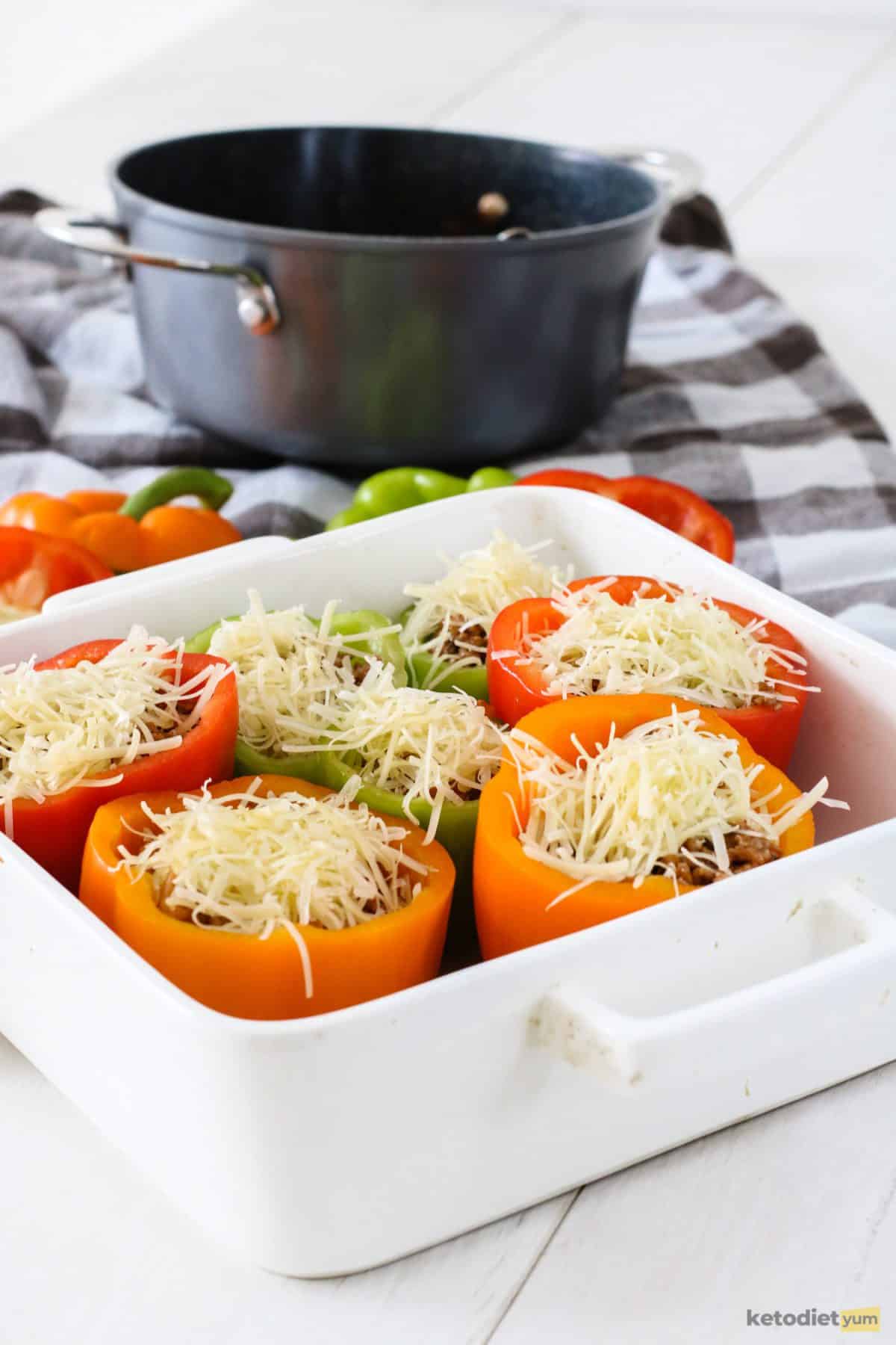 Bell peppers stuffed with ground beef, cauliflower and topped with Edam cheese in a baking pan ready to bake