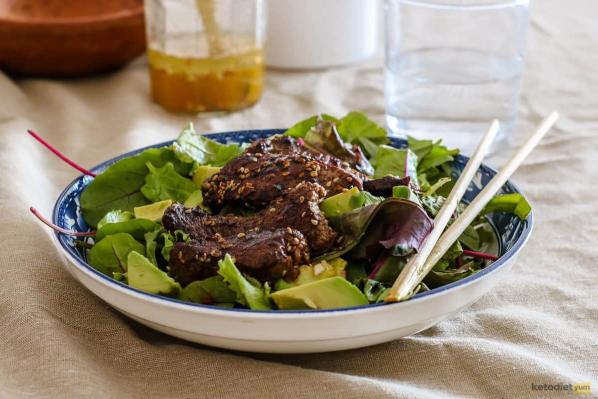 A delicious Korean BBQ Steak Salad with mixed greens, avocado and a sweet and spicy sauce served in a bowl with chopsticks