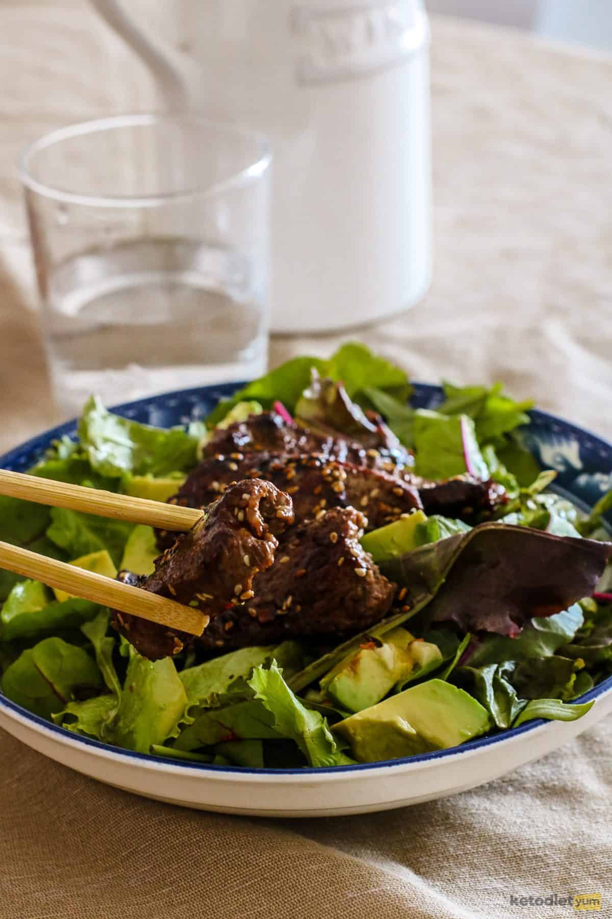 Delicious pieces of Korean BBQ steak on top of mixed greens and avocado drizzled with a sweet and spicy sauce