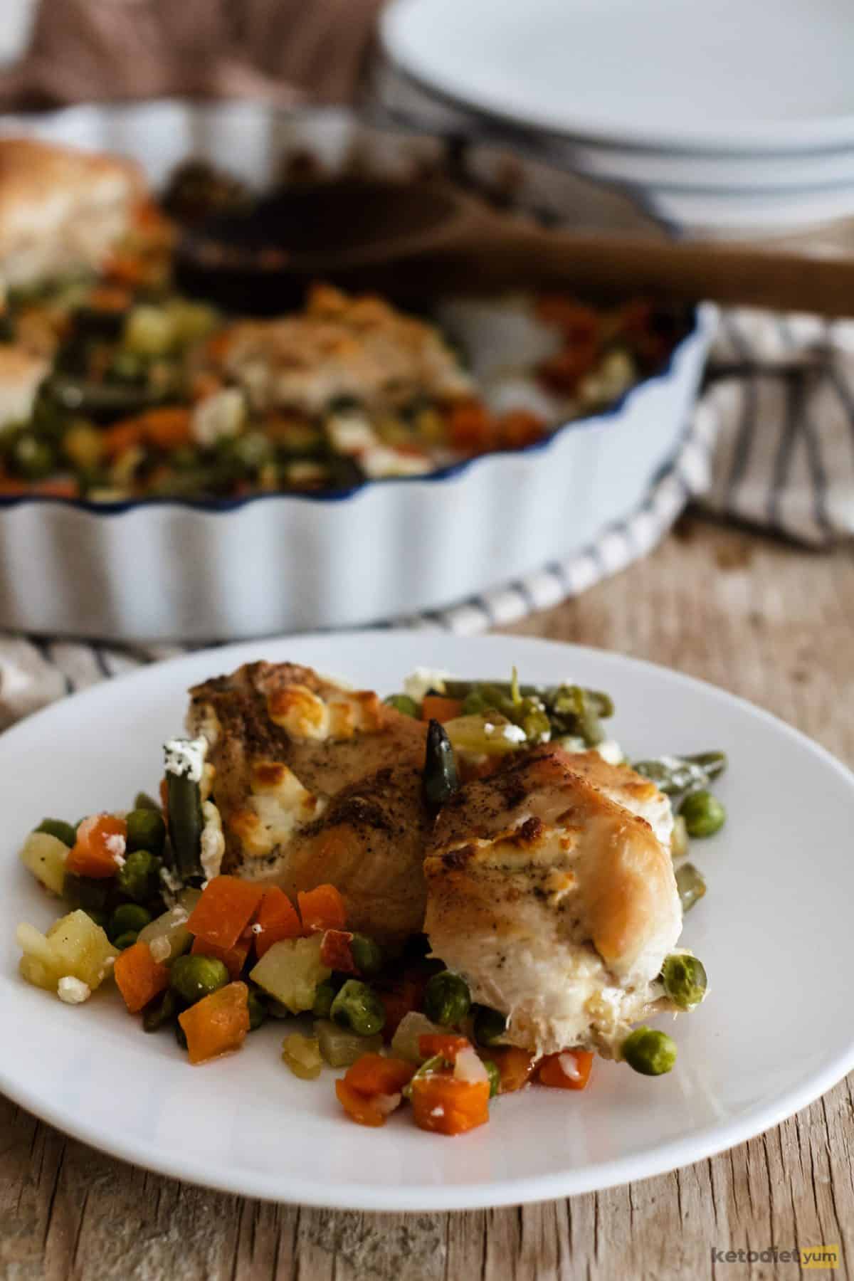 A portion of roasted chicken and vegetables with feta cheese served on a white plate