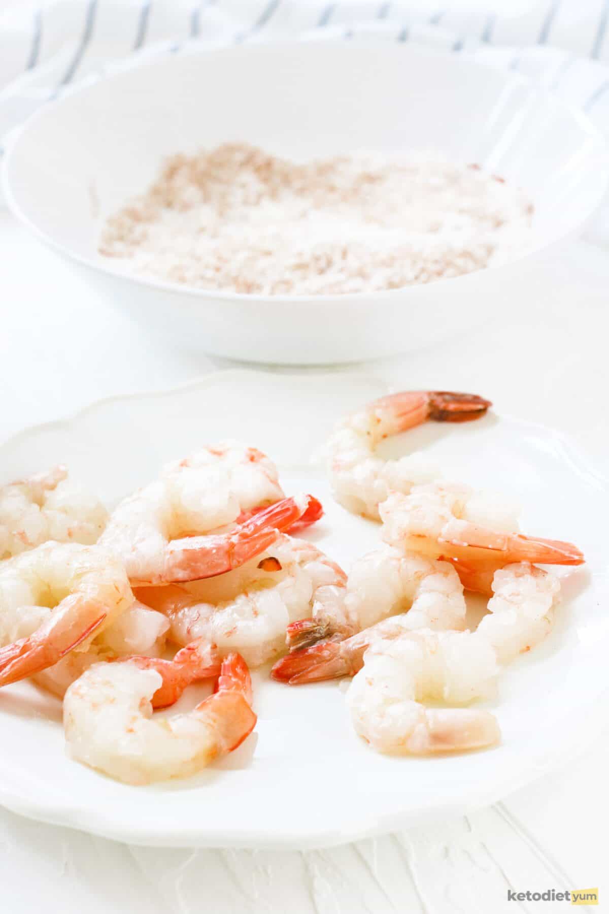 Shelled and deveined shrimp with the tails still on ready to be dipped in egg and coated with seasoned shredded coconut