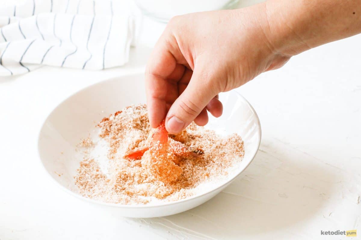 Holding shrimp by the tail and coating it in seasoned shredded coconut