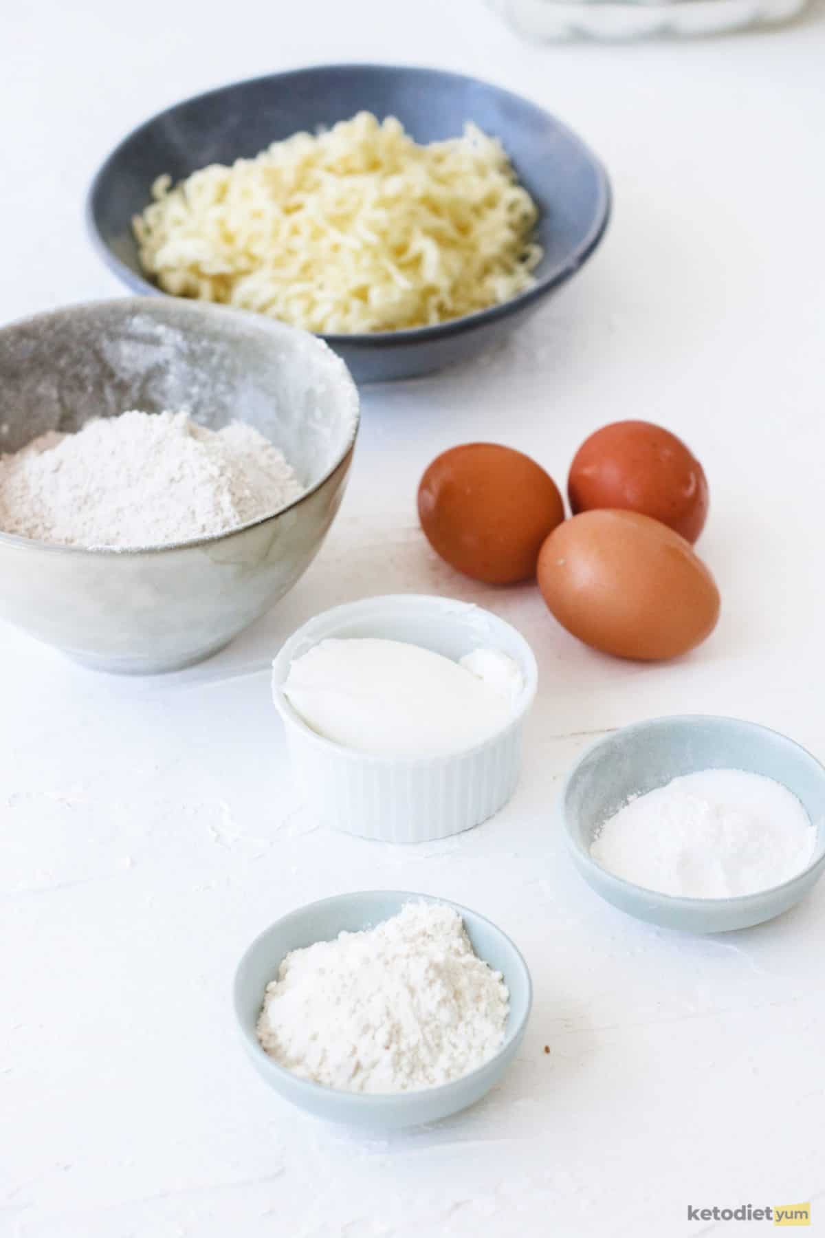 Ingredients arranged on a table to make keto bread rolls including almond flour, coconut flour, cream cheese, mozzarella, eggs and baking powder