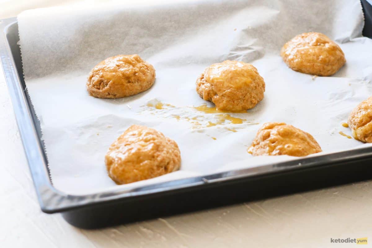 Keto bread roll dough rolled into balls and placed on a lined baking tray and brushed with egg wash