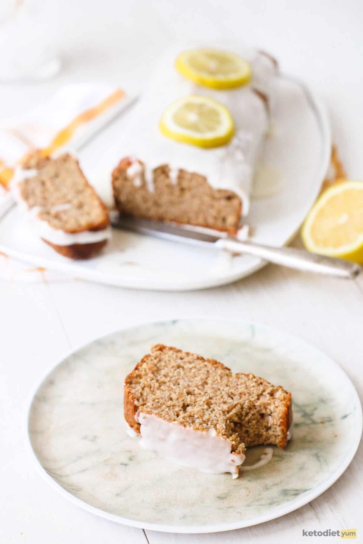 A slice of keto lemon pound cake on a plate with the whole loaf in the background