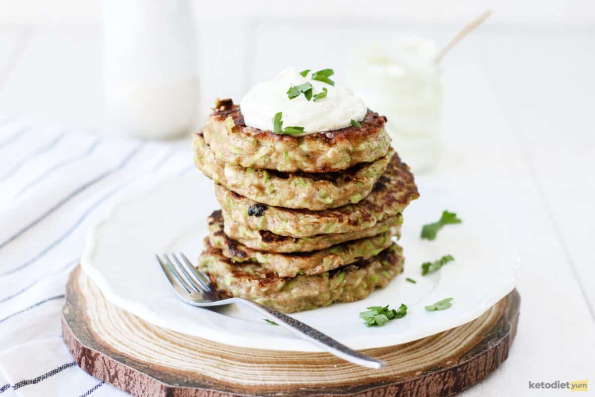 A stack of keto zucchini fritters served on a white plate topped with mayonnaise and freshly chopped parsley