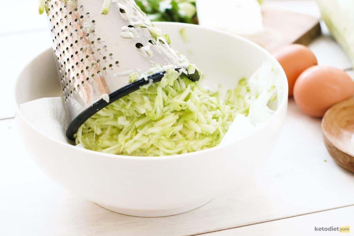 Grating zucchini with a cheese grater into a mixing bowl lined with baking paper