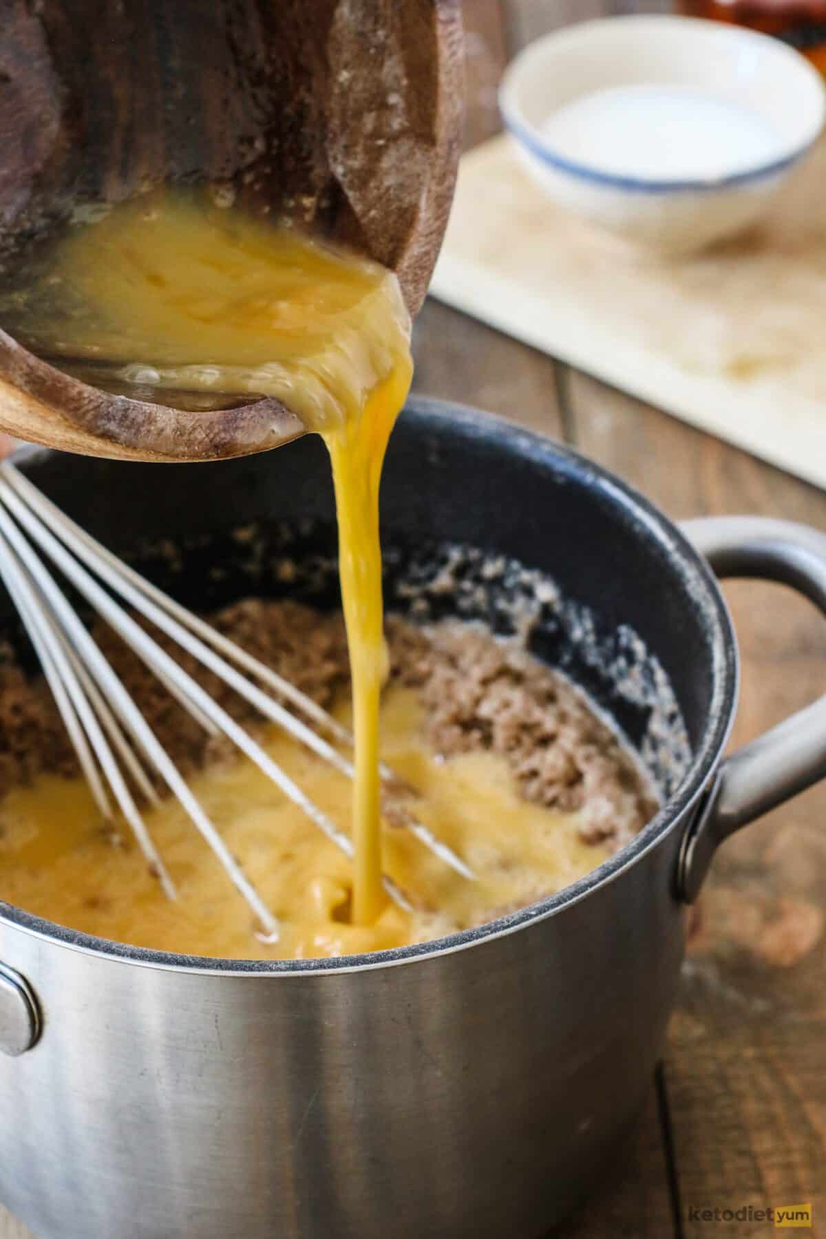 Adding whisked eggs to the donut hole dough to form an elastic dough ready to shape into balls