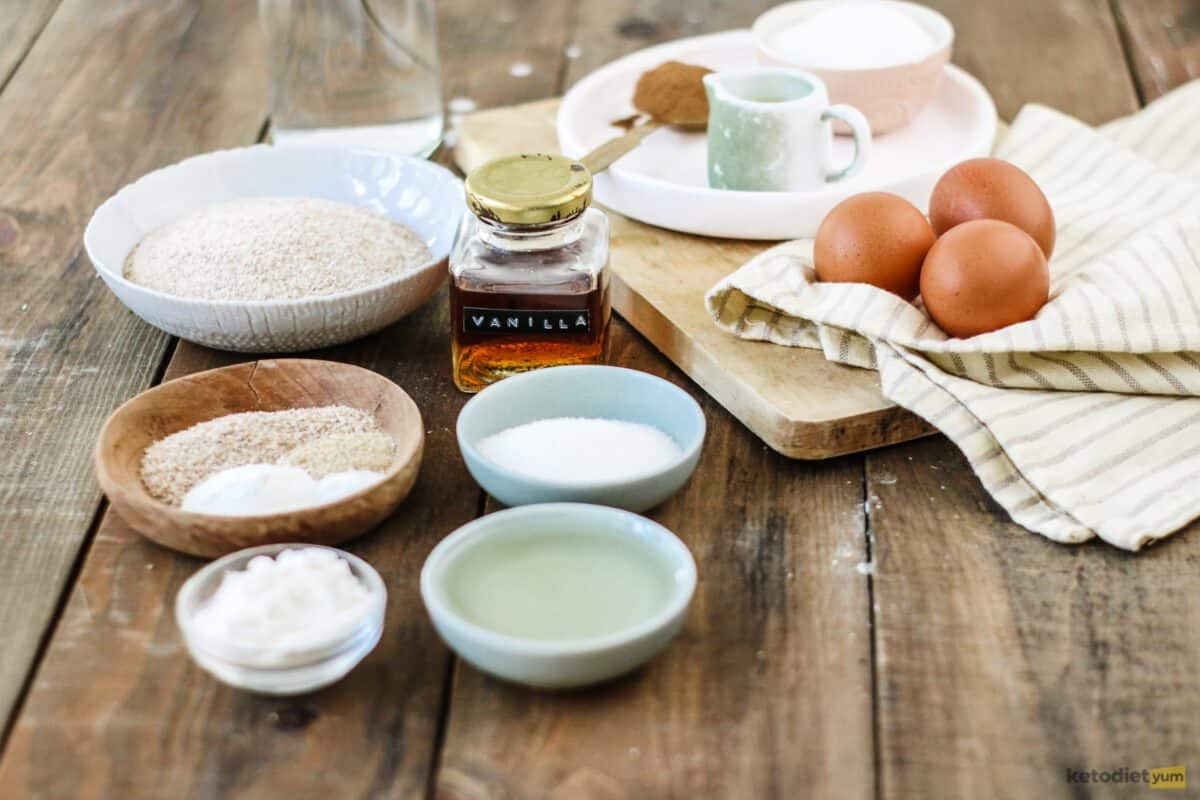 Ingredients arranged on a table to make keto donut holes including almond flour, eggs, vegetable oil, Erythritol, coconut flour, psyllium husk, xanthan gum, vanilla extract, baking powder, butter and cinnamon