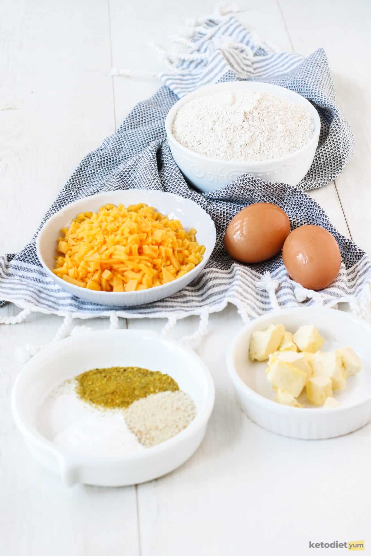 Ingredients arranged on a table to make keto cheddar biscuits including eggs, cheddar cheese, butter and almond flour