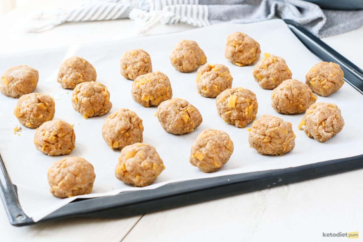 Keto cheddar biscuit balls arranged on a lined baking sheet ready to bake