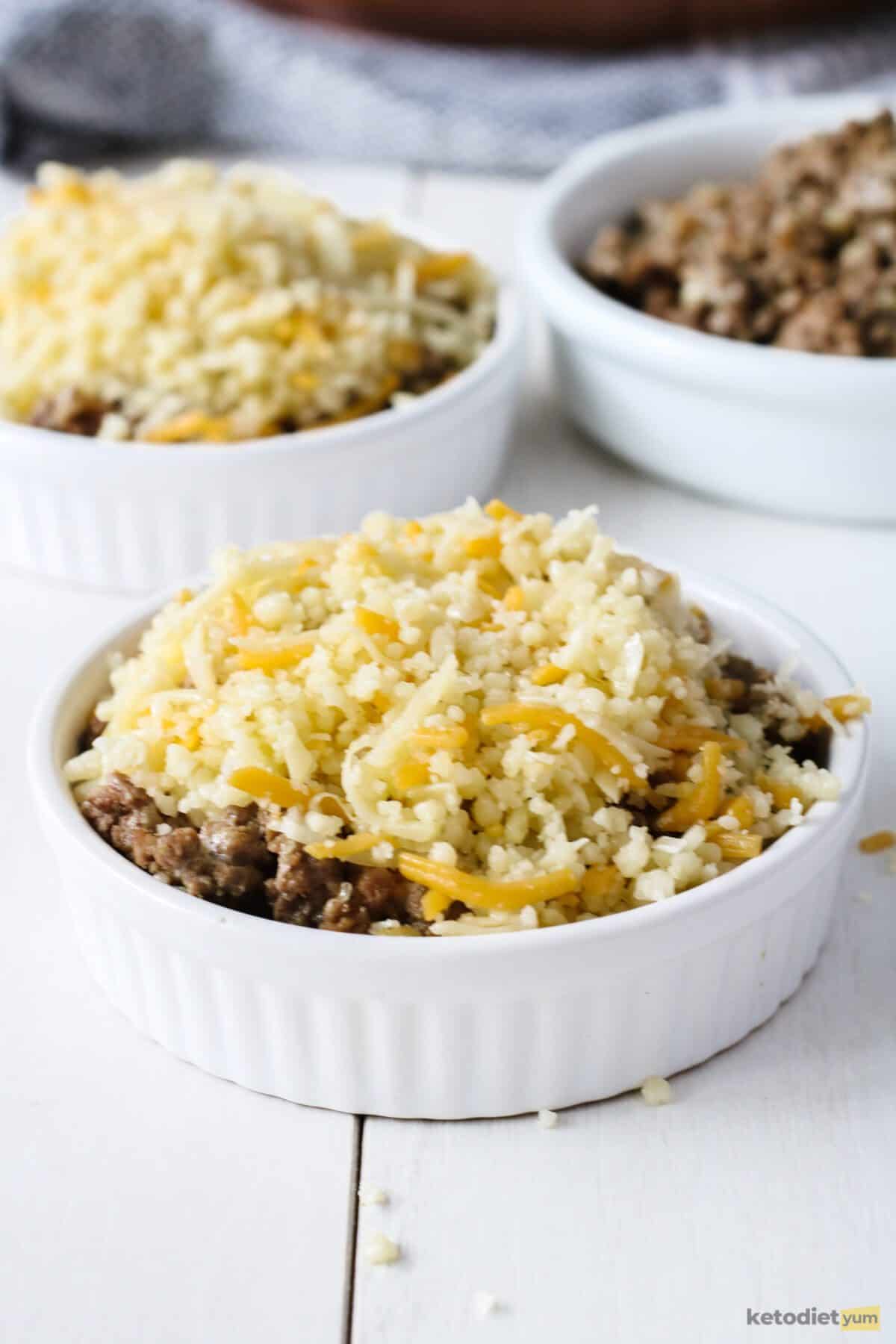 Mini keto cheeseburger pies topped with shredded mixed cheese ready to bake until golden