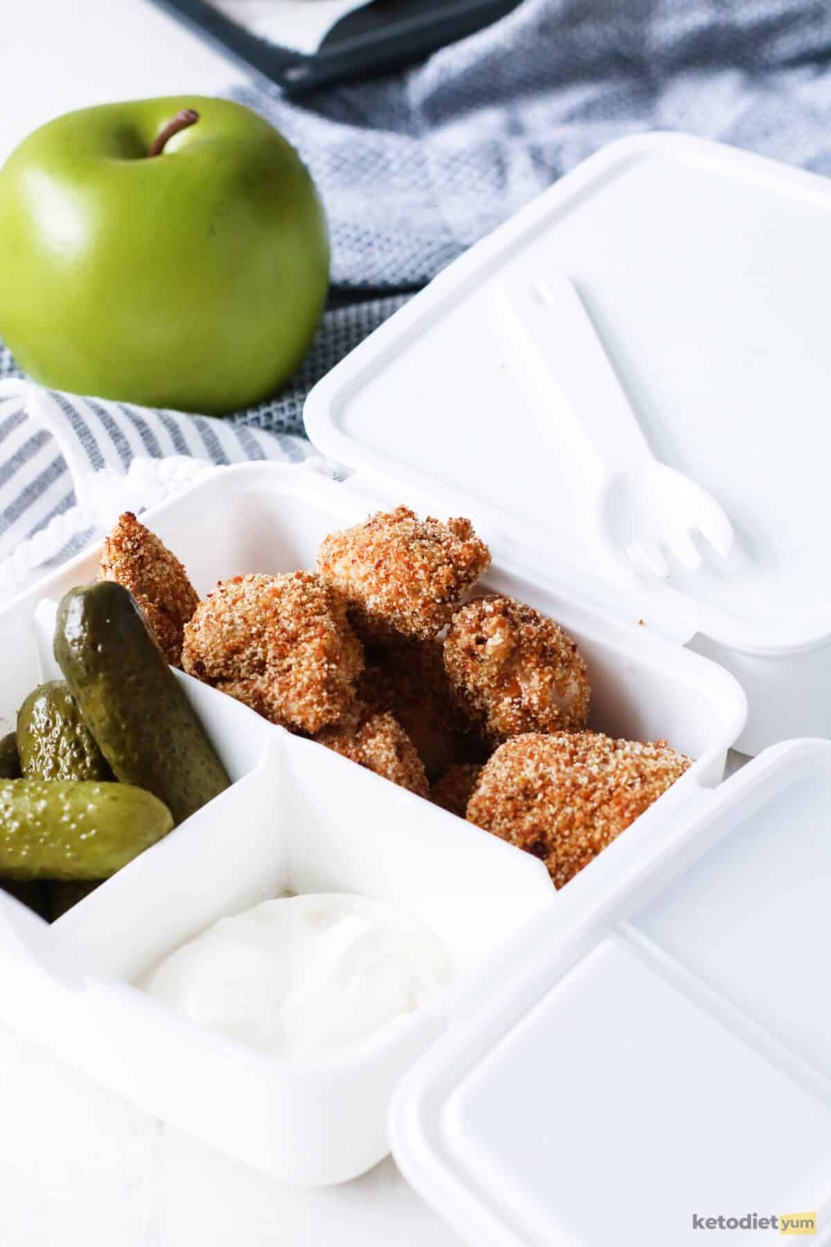 Keto chicken nuggets in a lunch box with dill pickles as a side and mayonnaise as a dip