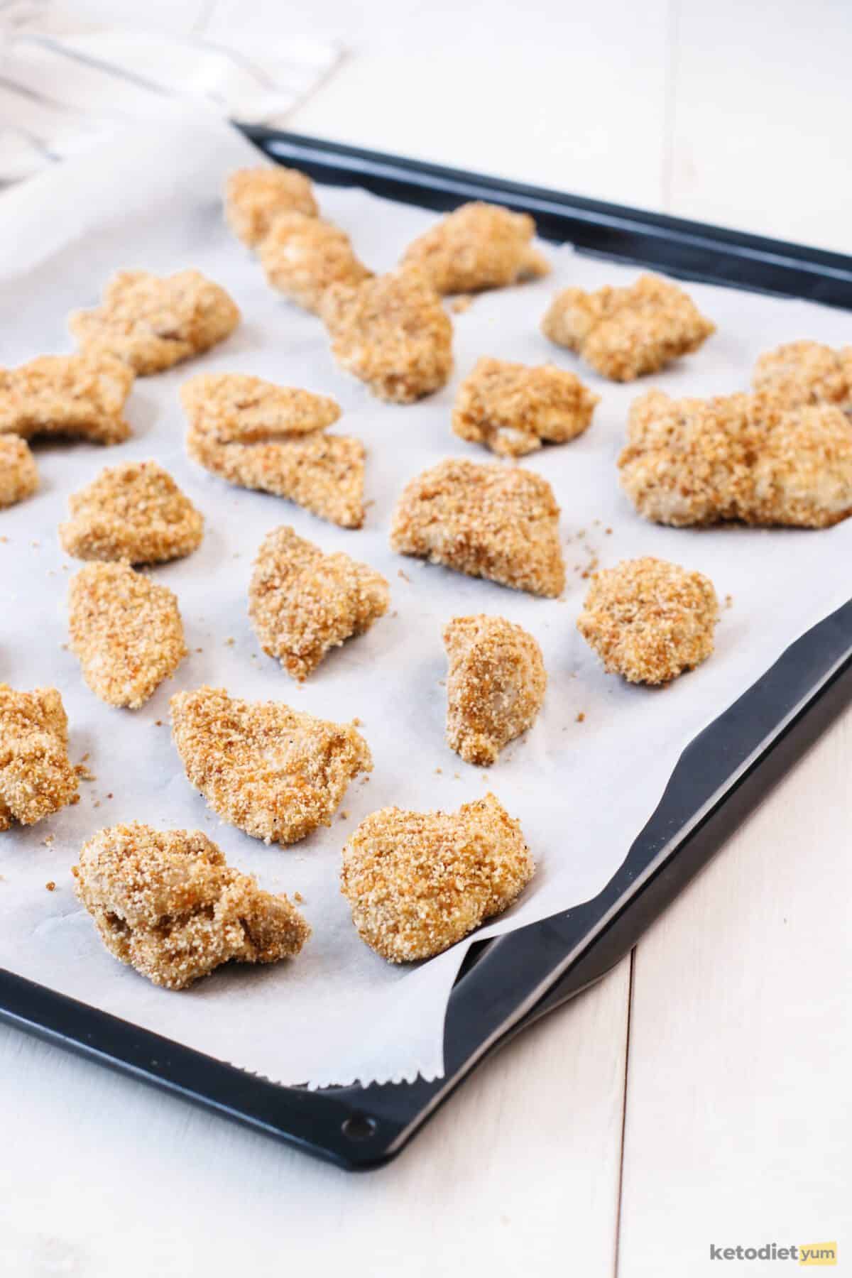 Keto chicken nuggets coated in a pork rind mixture and placed on a lined baking tray