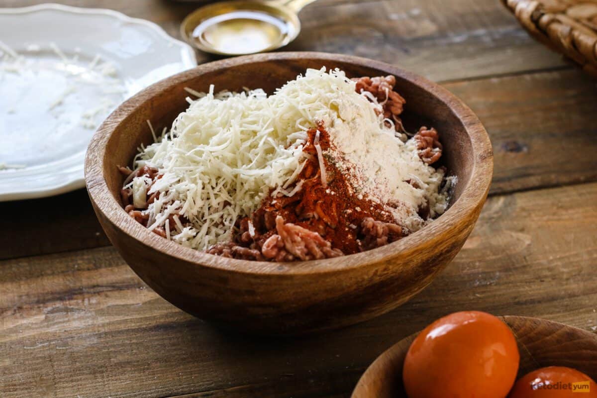 Combining ground pork, cheese, almond flour and seasonings in a mixing bowl to make Scotch eggs