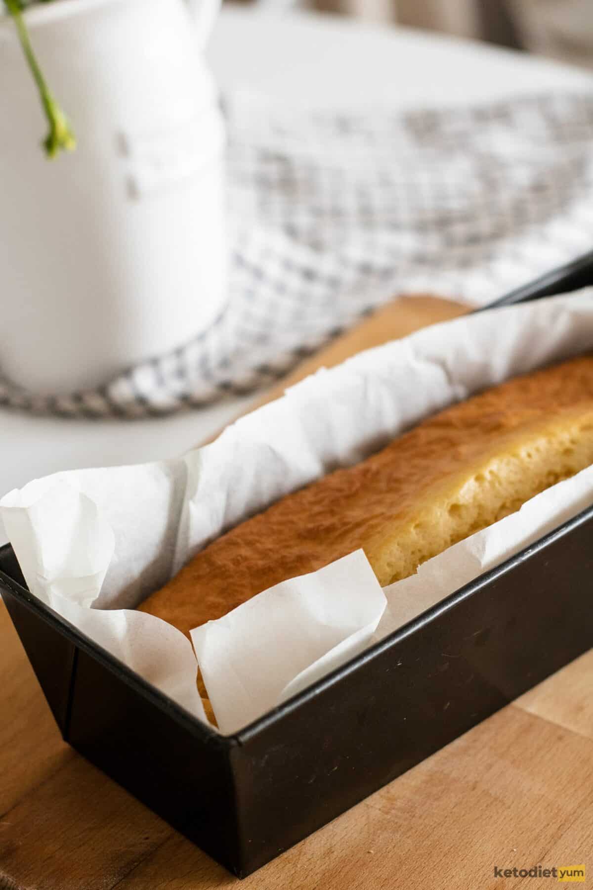 Lined loaf pan with golden loaf of bread on top of a brown wooden board