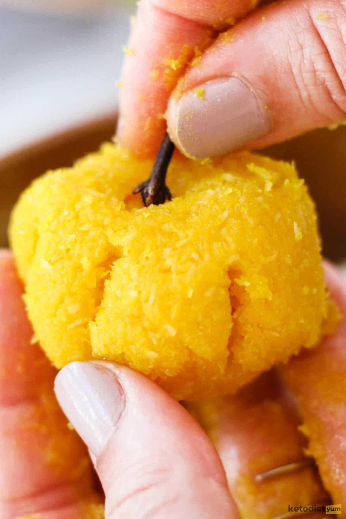 Hand holding a marzipan ball shaped into a pumpkin and placing a whole clove stick into the top as a decorative stem