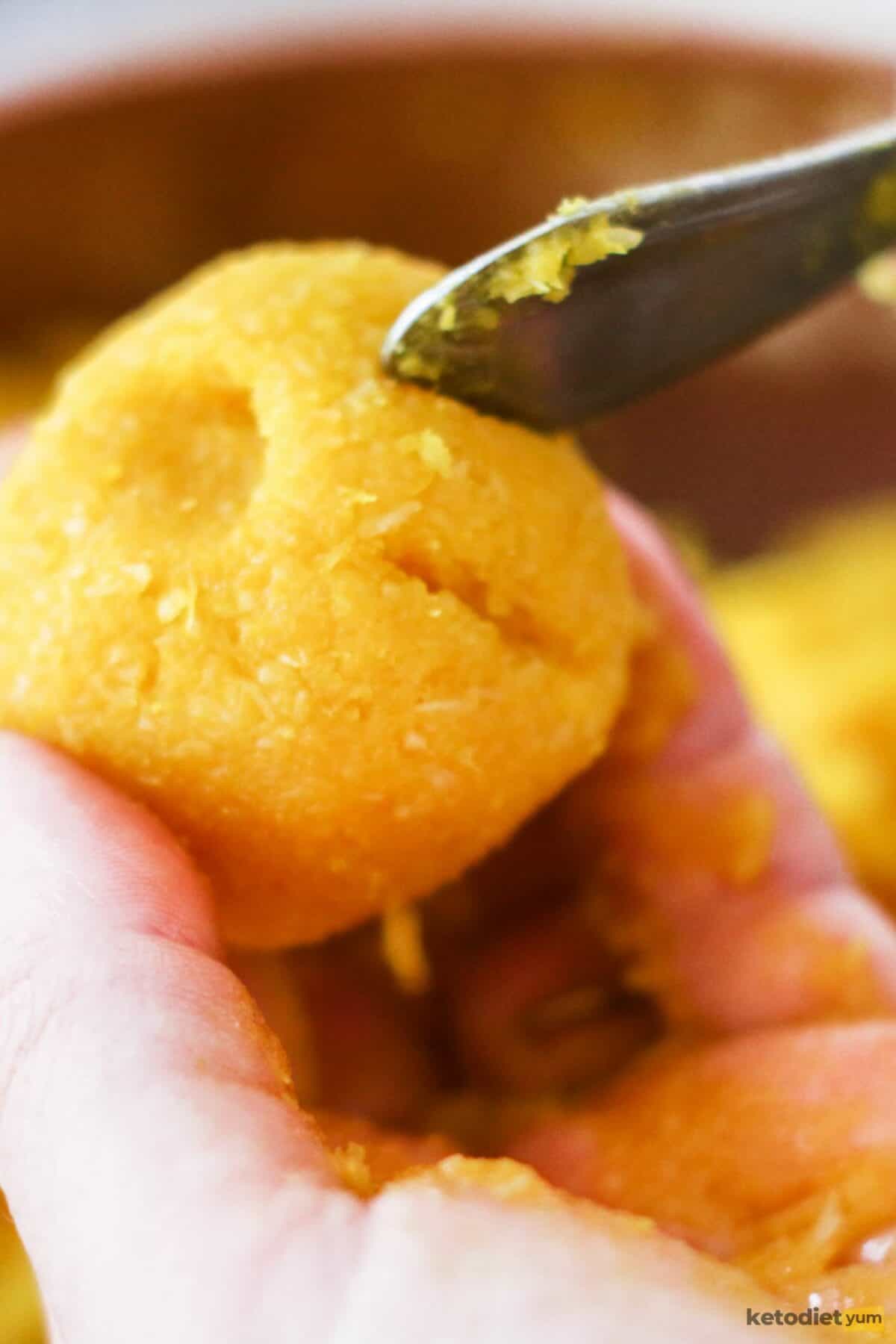 Hand holding a marzipan shaped pumpkin using the back of a fork to place decorative lines