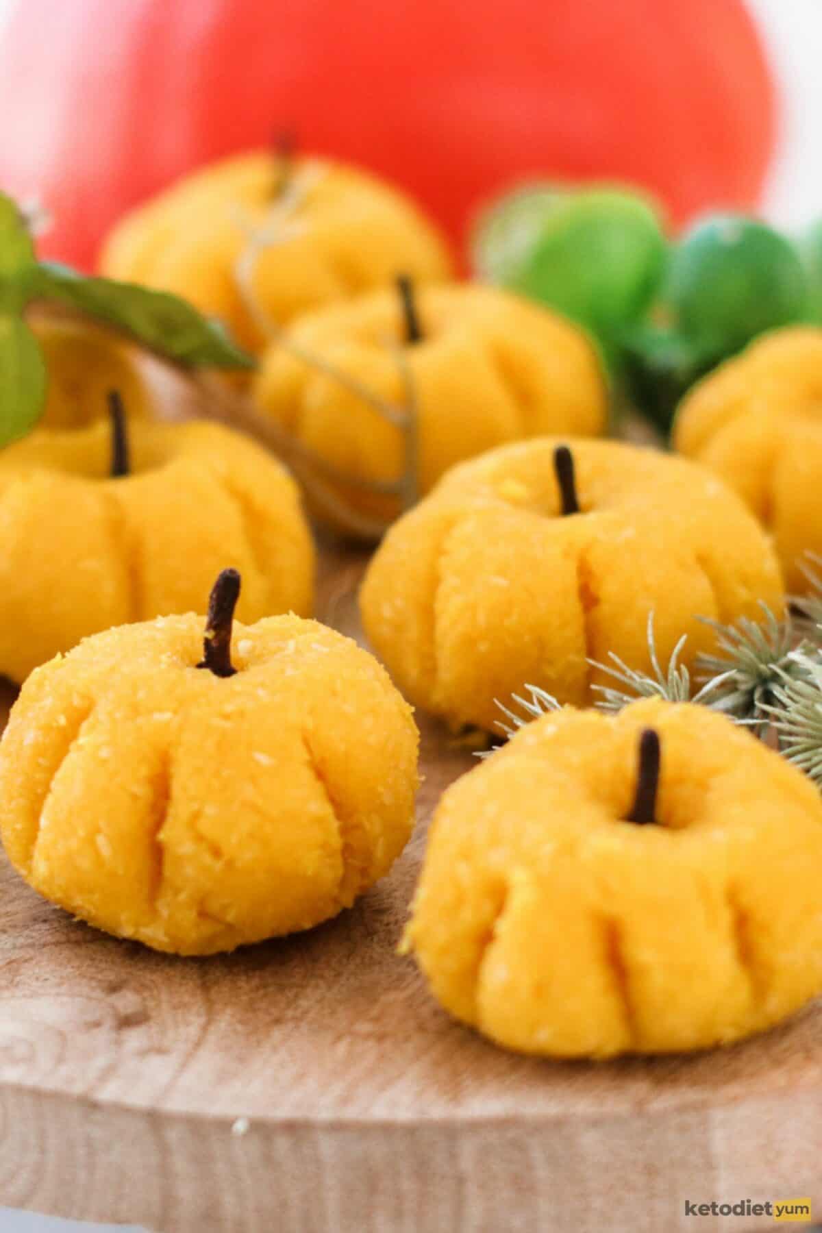 Marzipan pumpkins on a wooden board decorated with cloves and a pumpkin in the background