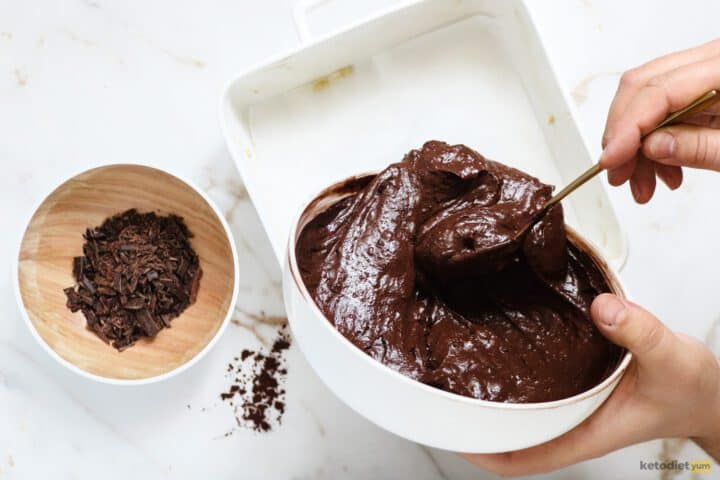 Pouring brownie batter into a baking pan with a bowl of chopped chocolate
