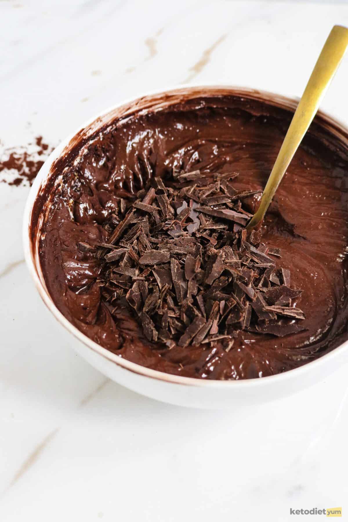 White bowl filled with brownie batter and chopped chocolate with a gold spoon inside