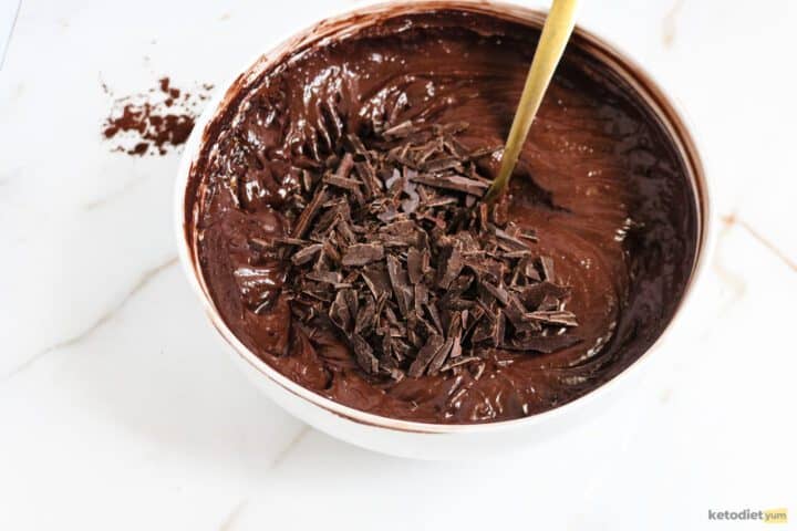 White bowl with brownie batter and dark chocolate pieces on top with a gold spoon