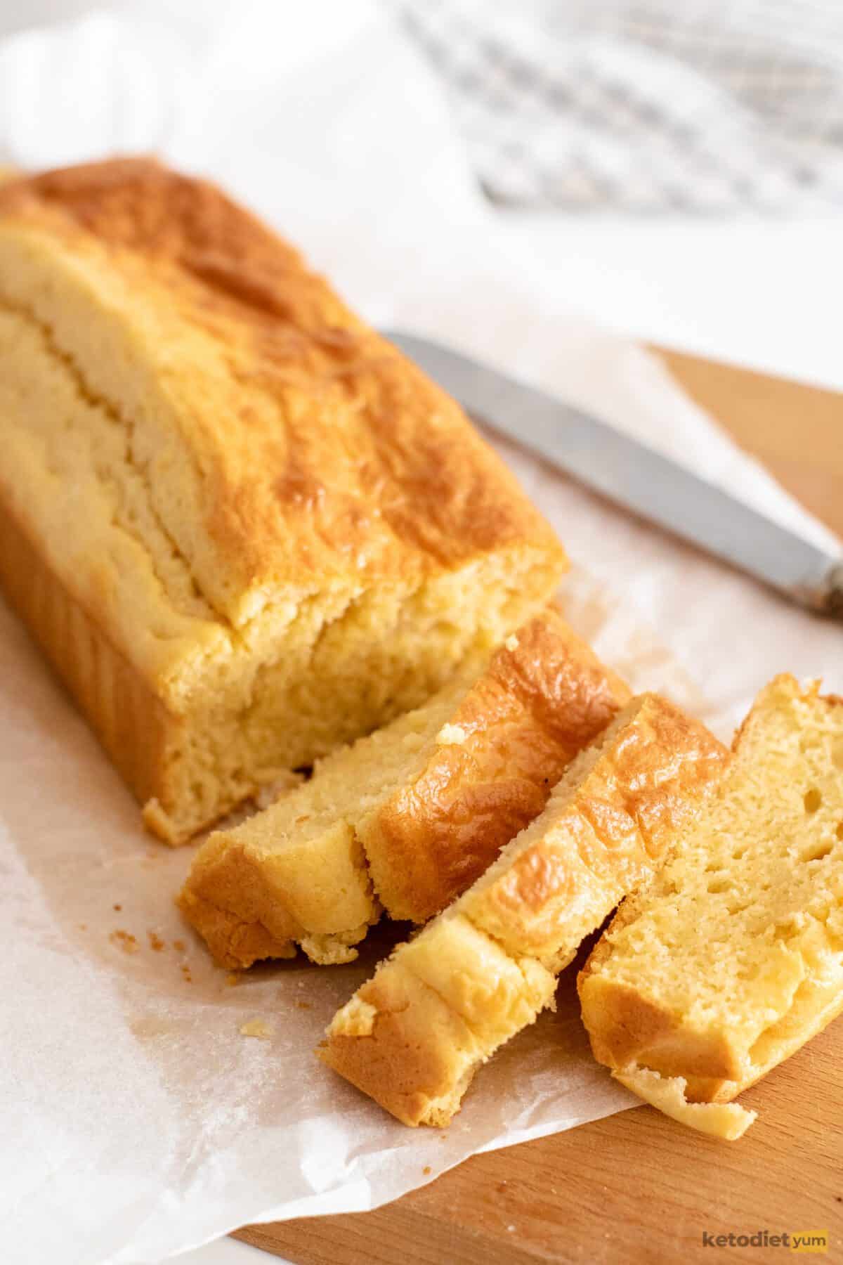 Loaf of bread on a wooden board under baking paper with 3 slices cut and a butter knife next to it