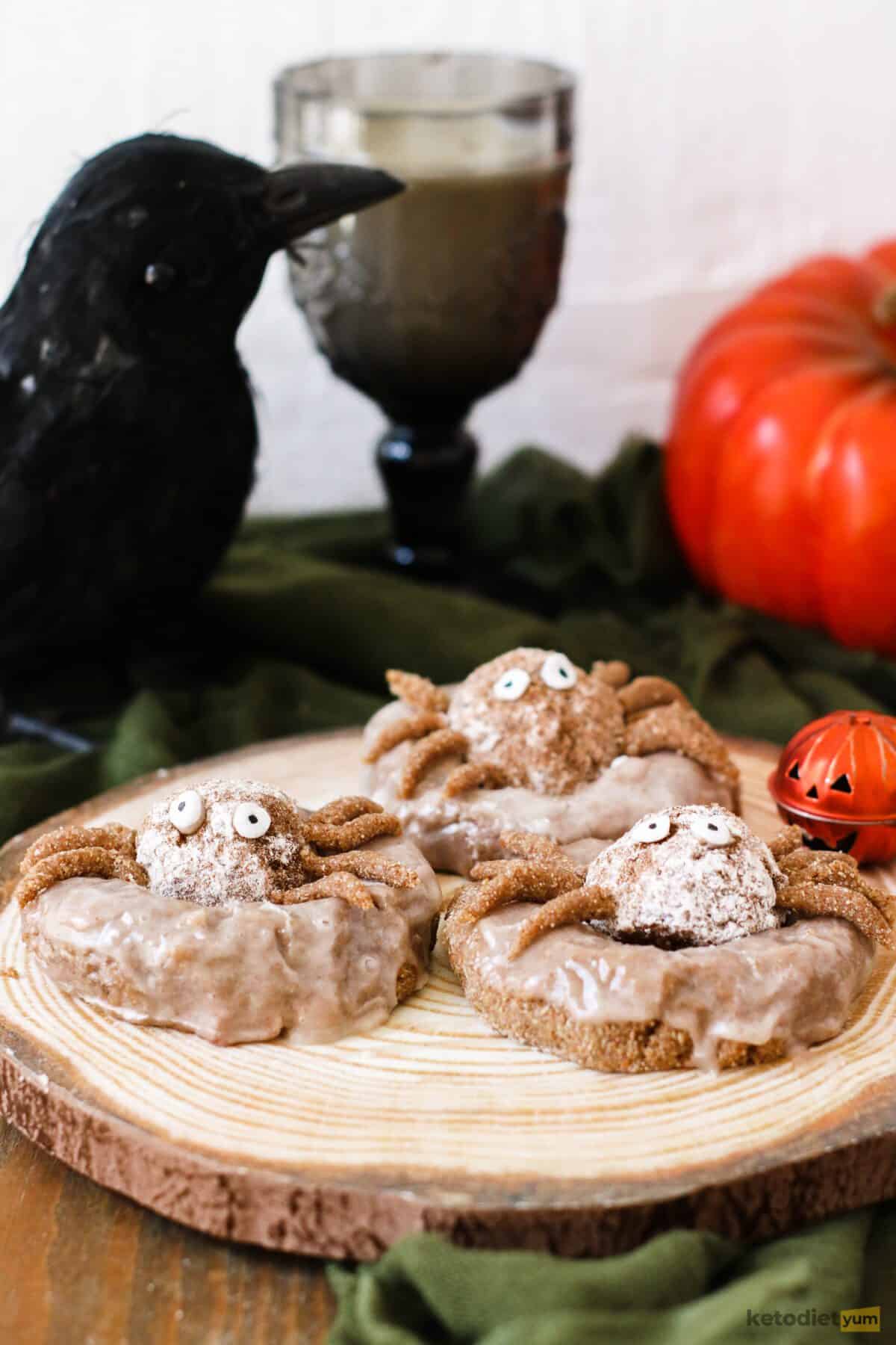 Three spider donuts with eyes and legs on table with Halloween decorations