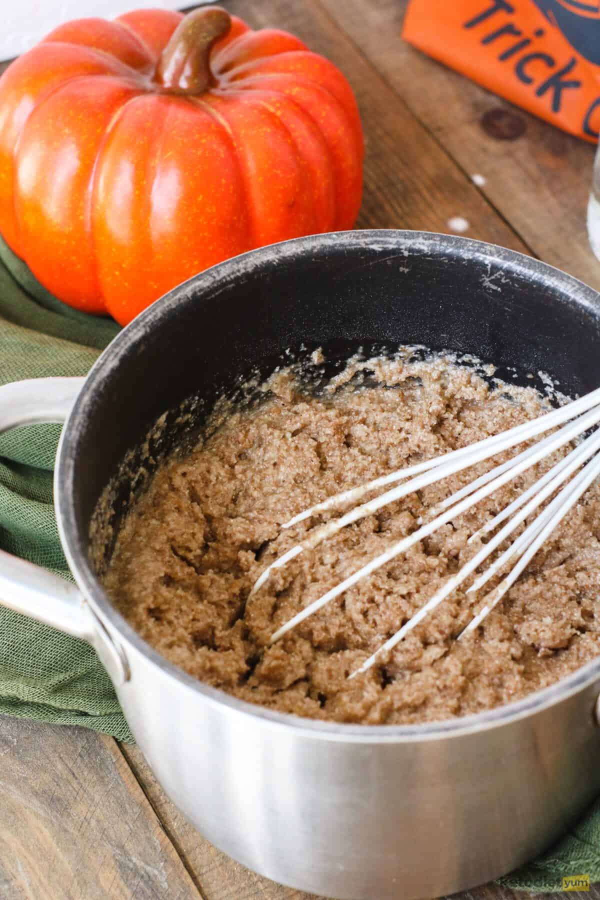 Small saucepan with dough and whisk on a table with a pumpkin in the background