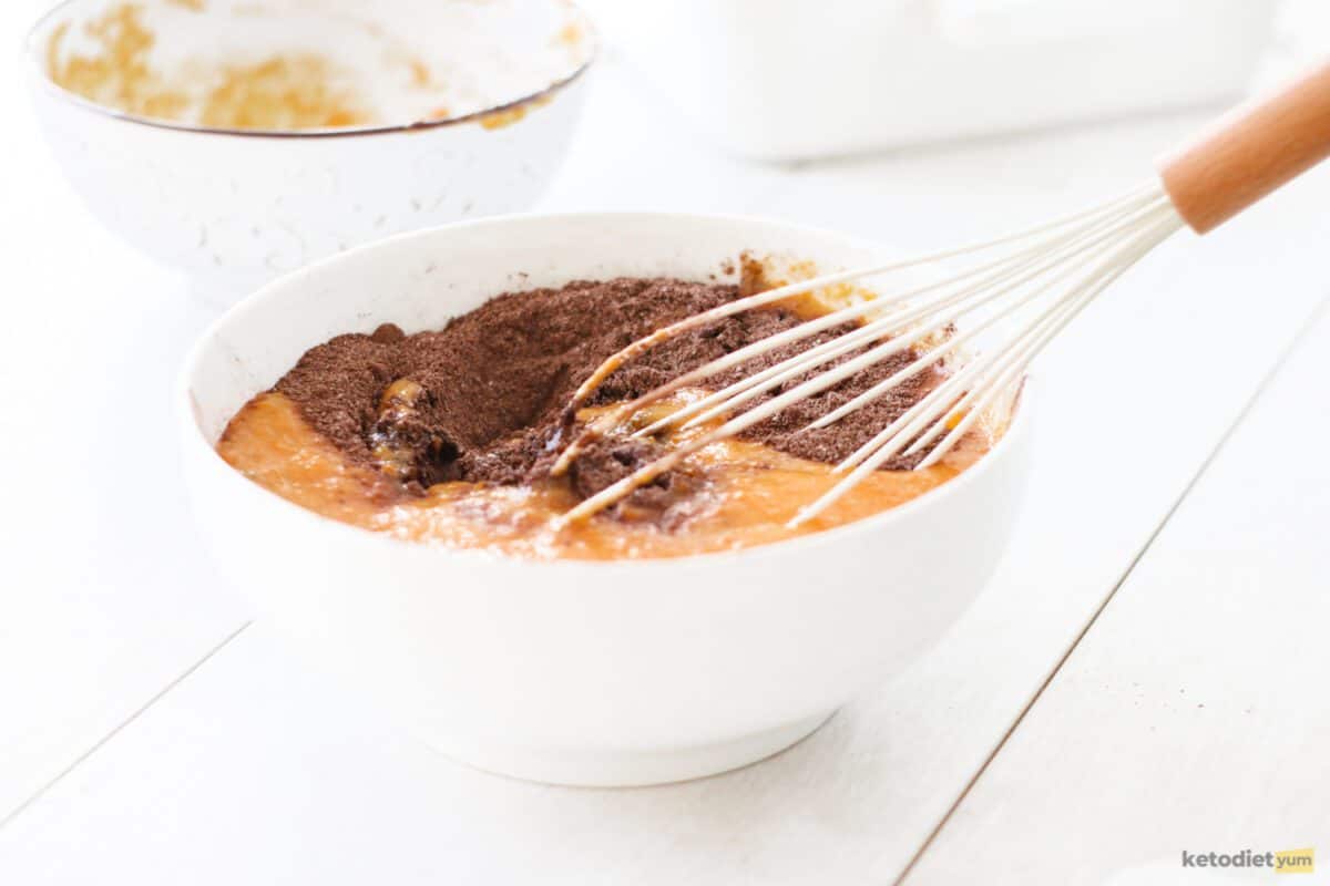 Wet and dry ingredients in a white bowl with a whisk and another bowl in the background