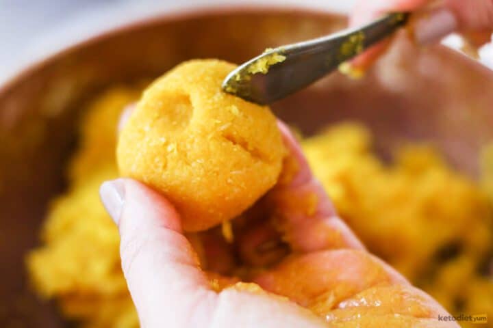 Orange dyed marzipan ball with the back of a fork carving lines into it so it looks like a pumpkin