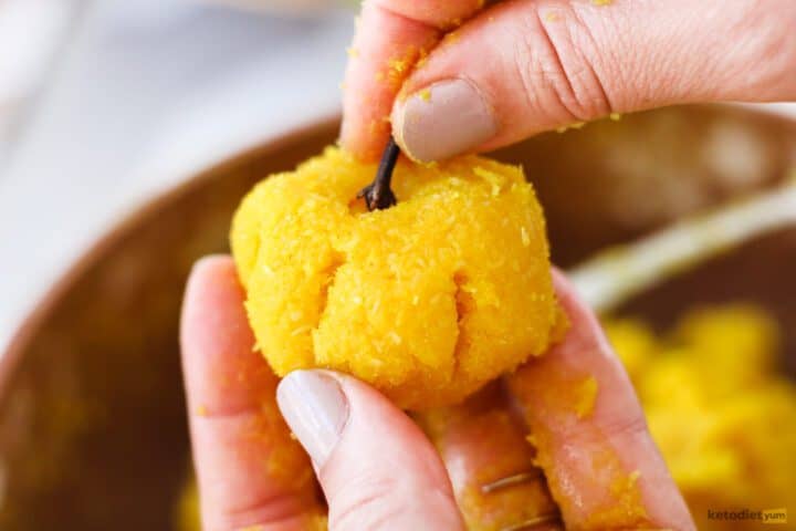 Cute marzipan ball shaped into a pumpkin with a whole clove used as the pumpkin stem