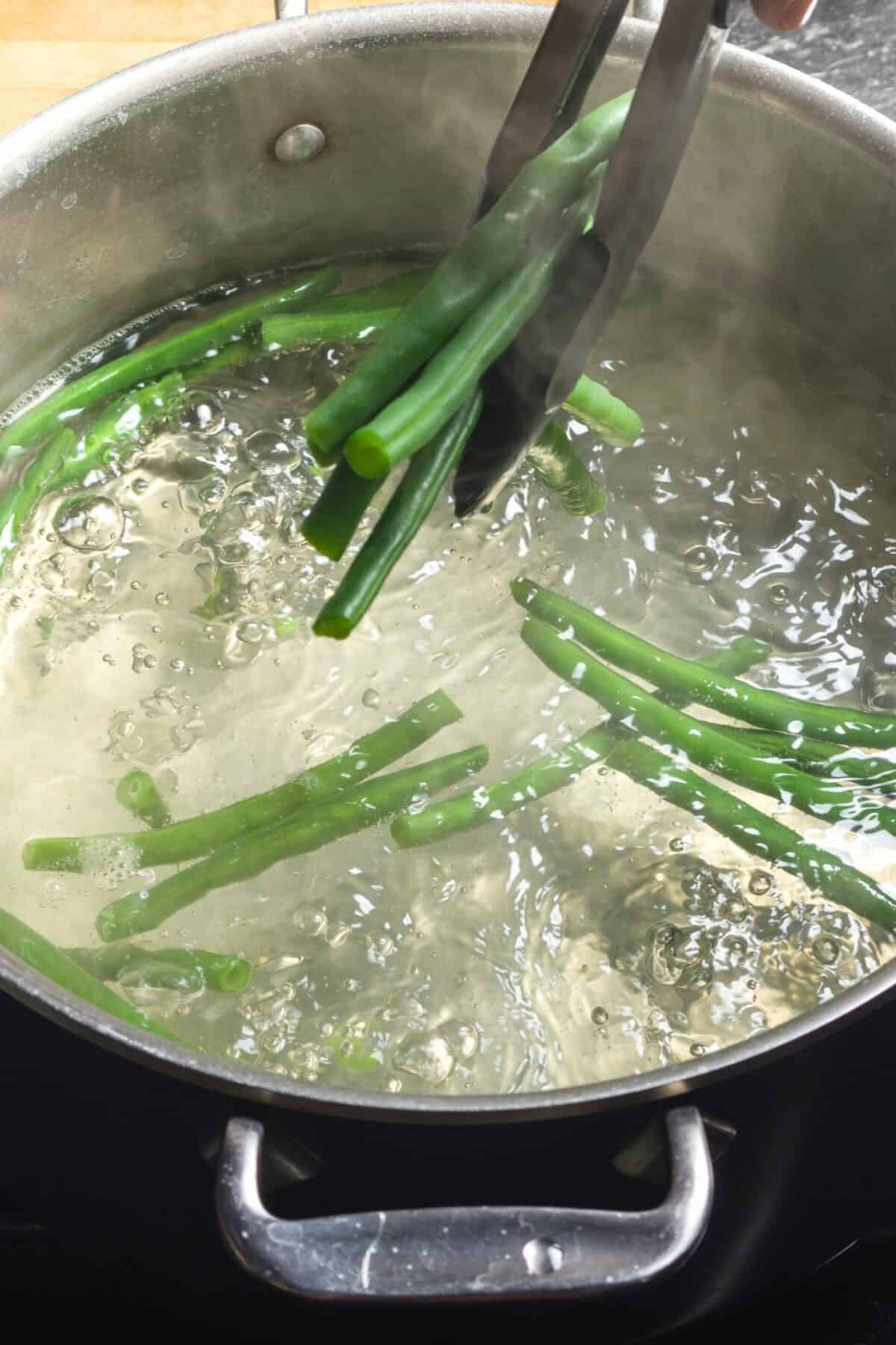Blanching green beans in a pot of boiling water before drying and seasoning