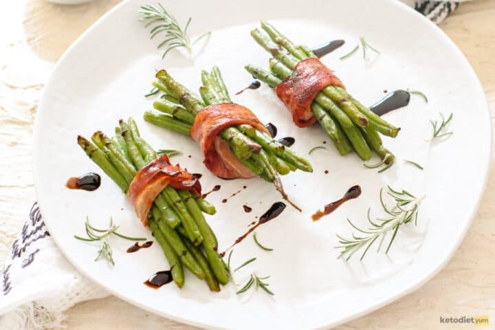 Three portions of bacon wrapped green beans on a plate drizzled with balsamic vinegar