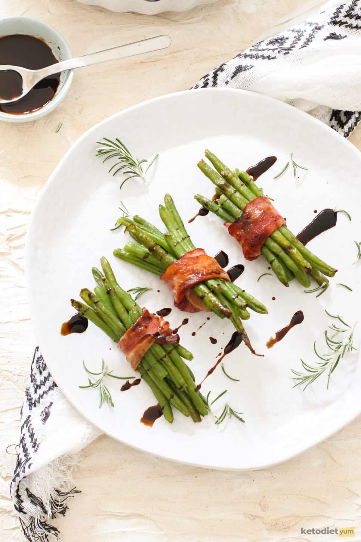 3 bundles of bacon wrapped green beans drizzled with balsamic vinegar and served on a white plate