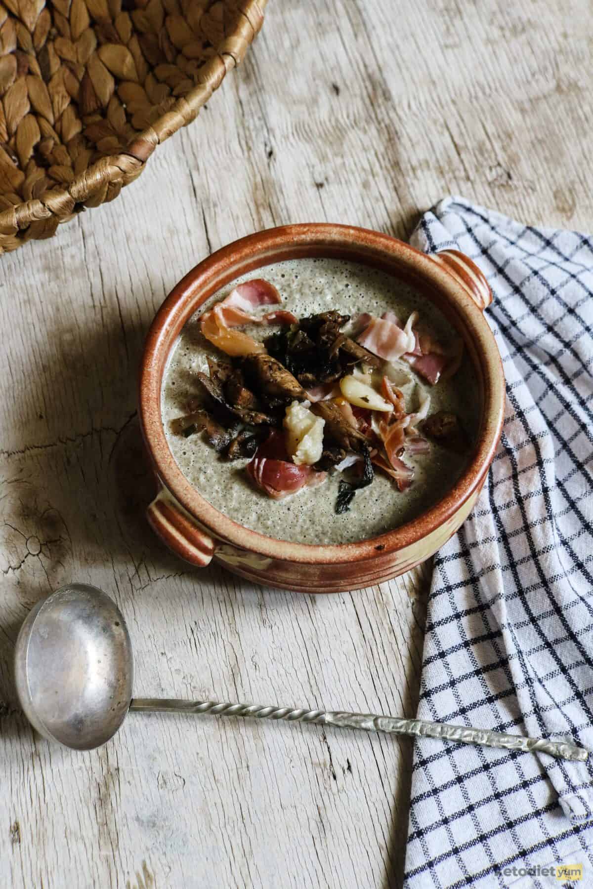 Bowl of mushroom soup on a table with a ladle and kitchen towel 