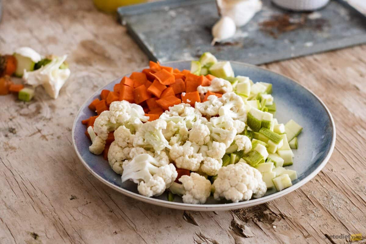 Plate with cauliflower florets, diced zucchini and diced carrot on a wooden table