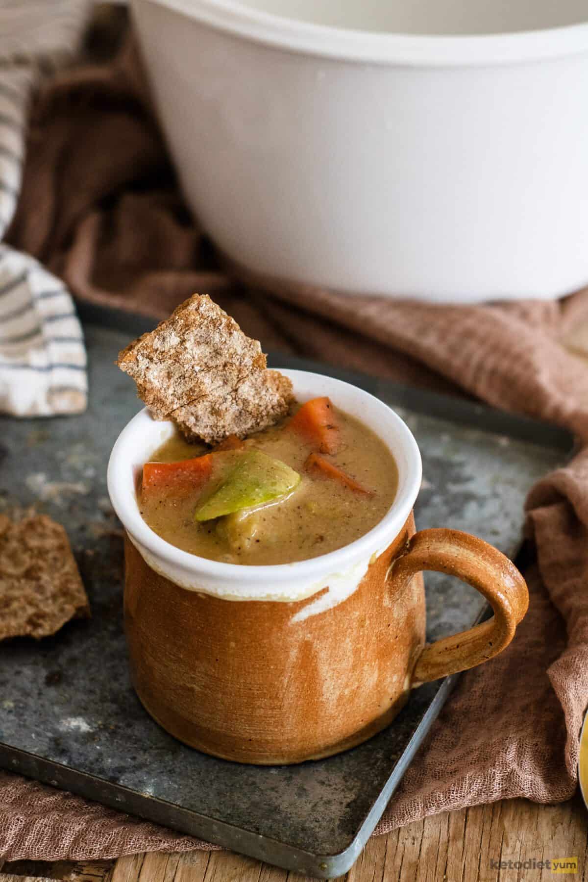 Mug filled with keto veggie soup served with a low carb cracker
