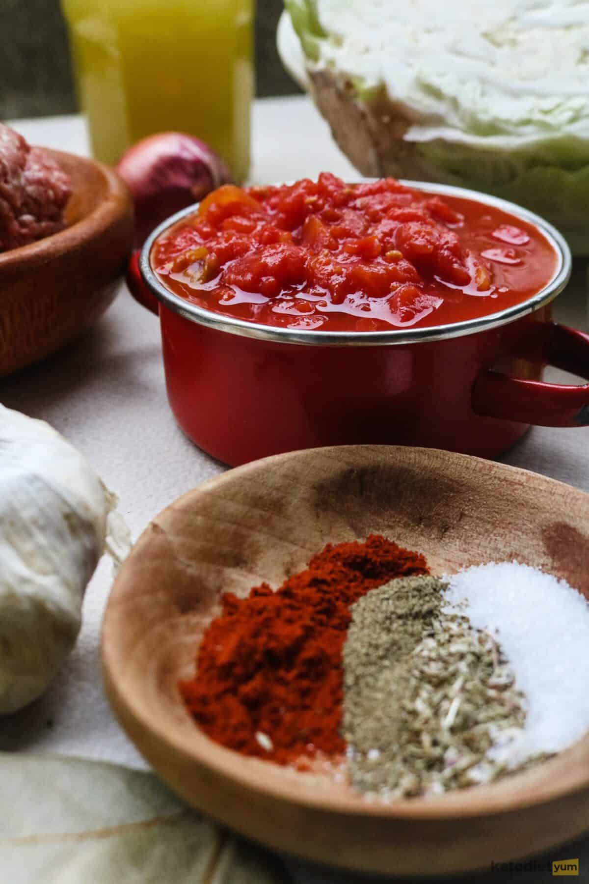 Bowl of herbs and spices and bowl of crushed tomatoes on a table with a cabbage in the background