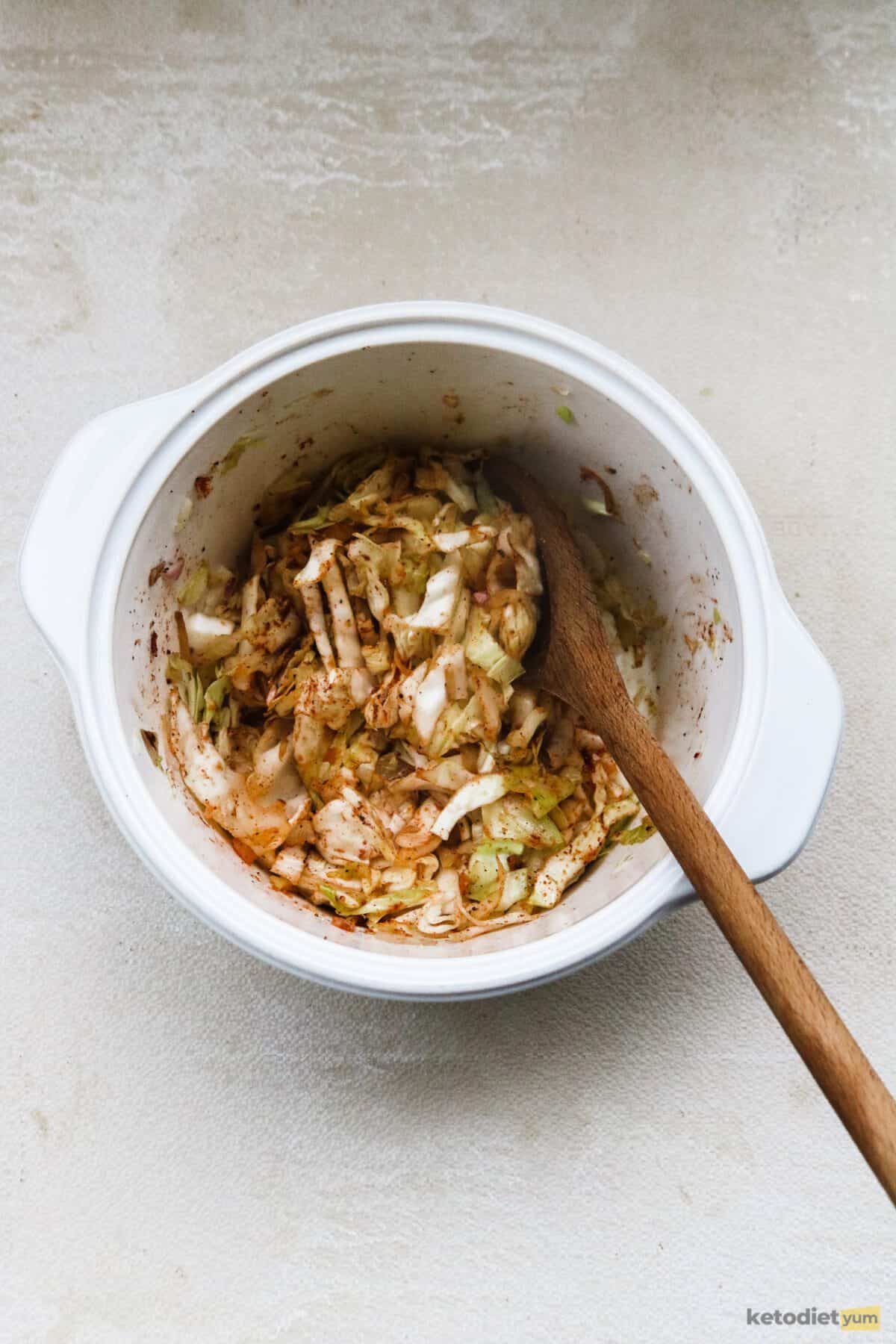 Saluted cabbage, onion and ground beef with seasonings in a pot with a wooden spoon inside