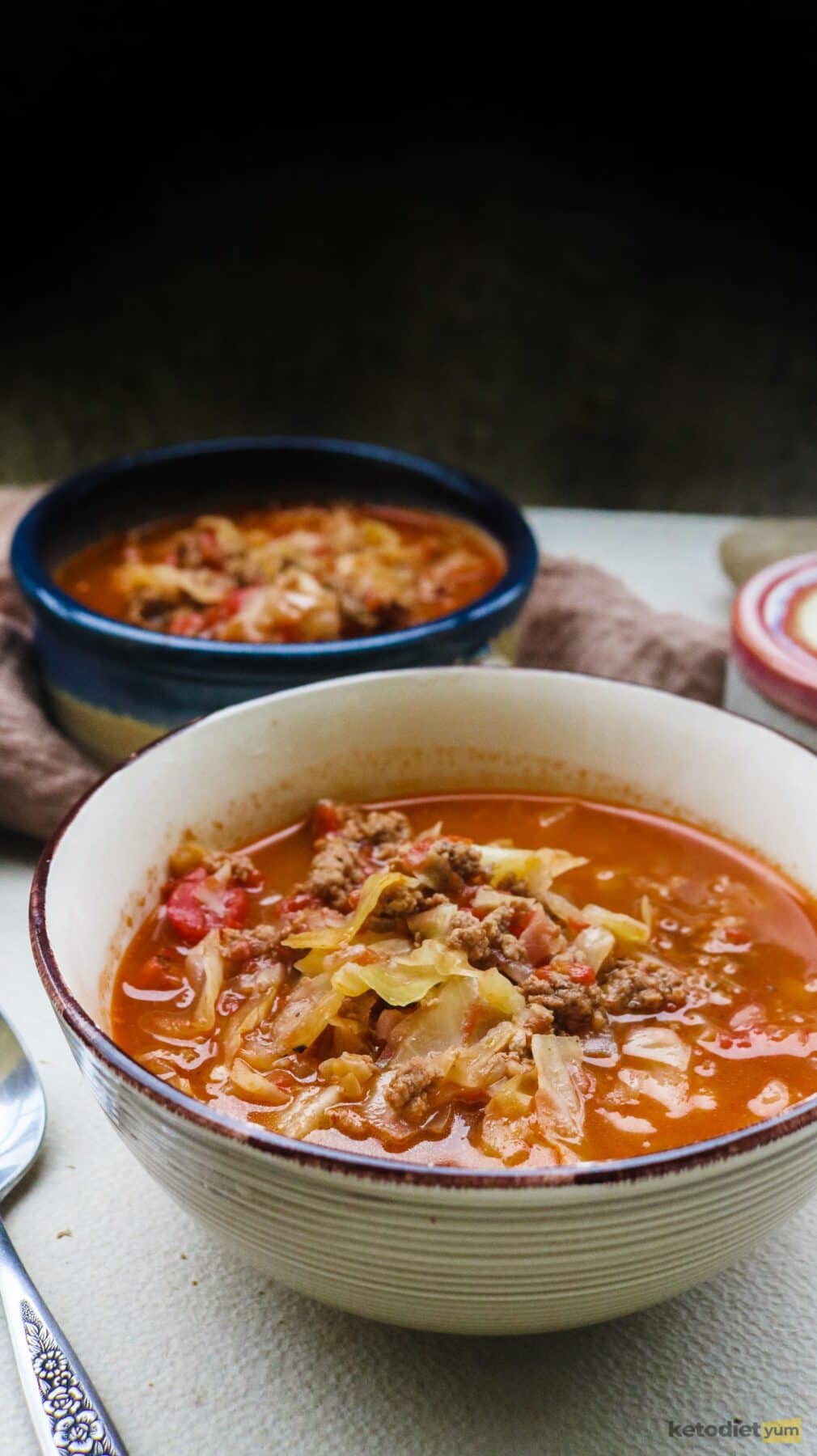Close up bowl of tomato cabbage soup with ground beef on a table with a spoon