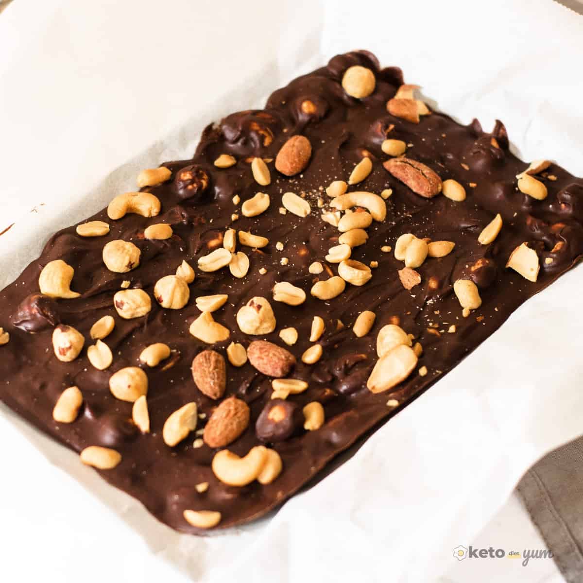 Keto chocolate bars with mixed nuts in lined baking pan